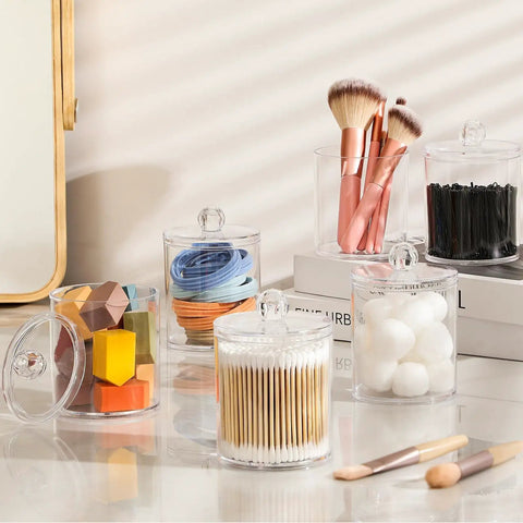 Super Practical Four Pack Clear Acrylic Qtip Holder Dispensers With Lids For Organizing Cotton Swabs Balls Pads And Floss Picks Comes With Labels In Two Sizes Twelve Ounce And Ten Ounce displayed with various bathroom items.