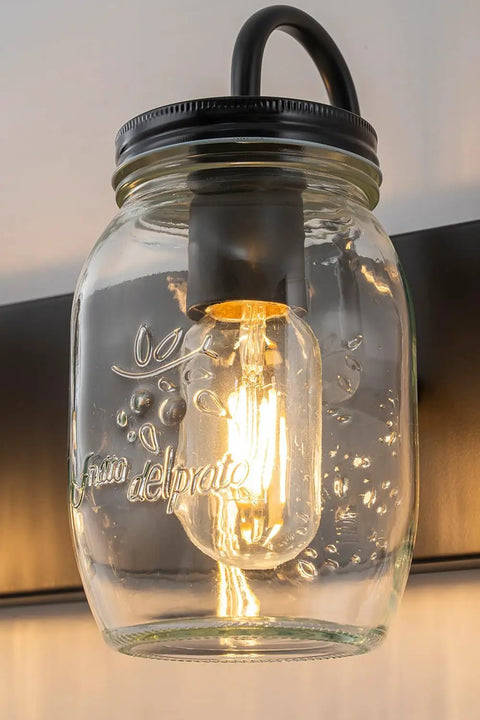 Close-up of a mason jar vanity glass wall light with exposed bulb, part of black wall sconce for farmhouse decor.