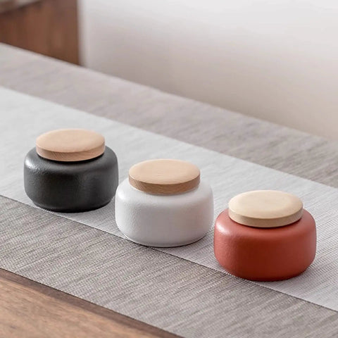 Handcrafted Ceramic Tea Canisters With Airtight Wooden Lids Keep Your Daily Stash Locked In This Rock Solid Porcelain Storage Set Of Four For Modern Home Kitchens. Three jars in black, white, and red on a table.