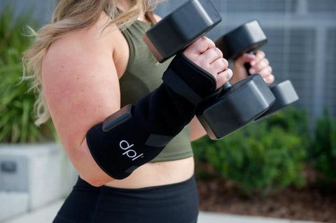 Woman using a Red Light Therapy Wrist Wrap for Pain Relief and Carpal Tunnel Support, lifting dumbbells outdoors.