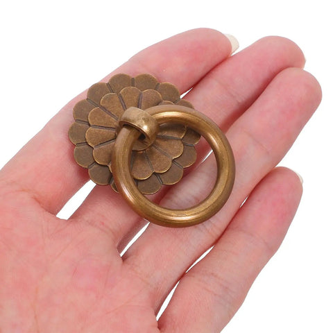 Close-up of a vintage brass ring pull handle for cabinets from six piece set, showing antique bronze finish detail on a hand