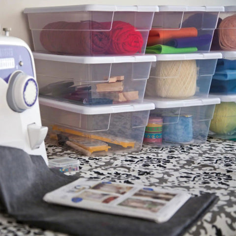 Slick Stackable Clear Plastic Storage Bins 6 Quart Capacity 12 Pack holding yarn, craft supplies near a sewing machine.