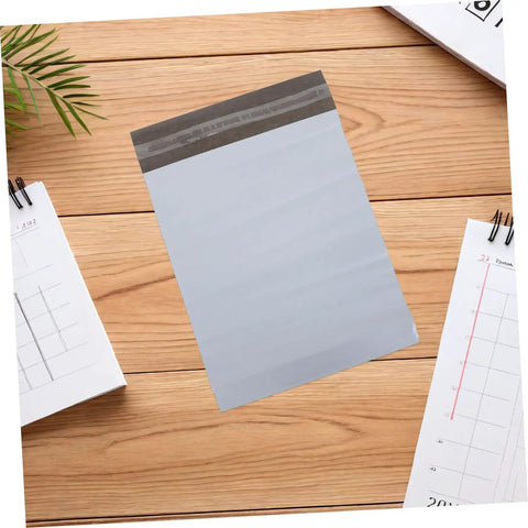 White Poly Mailer Bags 100 Pack 10x14 Inch Waterproof Self Seal Envelopes on wooden surface with calendars