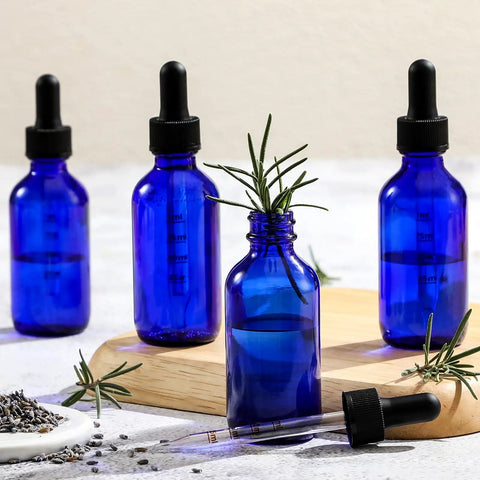 Dead Simple 2 Oz Dark Blue Glass Dropper Bottles, 4 Pack With Exact 1Ml Calibrated Eyedroppers, No Drama Silicone Caps For Essential Oils displayed with herbs.