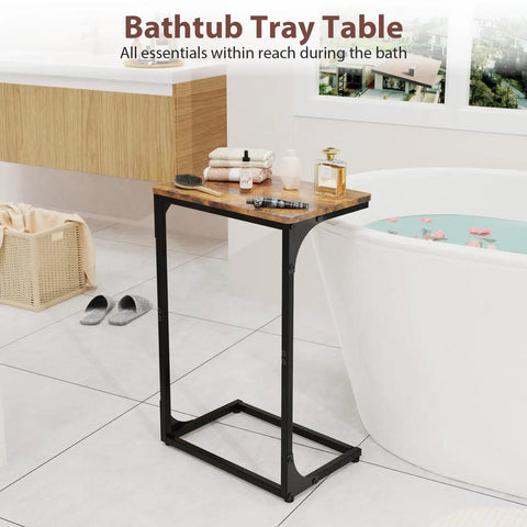 Bathtub tray table next to white bathtub in bathroom, featuring wooden top and black metal frame, holding toiletries and candle