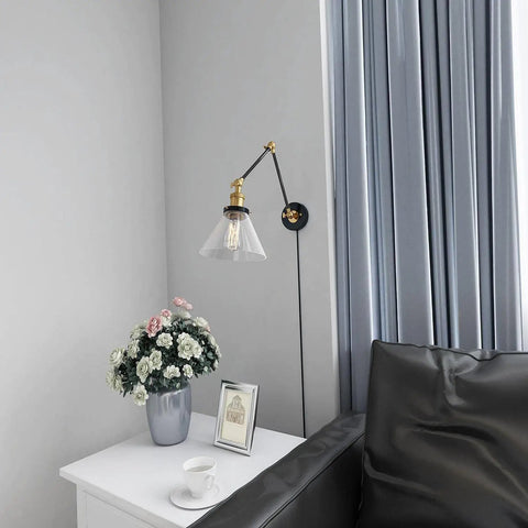 Black And Gold Glass Swing Arm Wall Sconce above white table with flowers, Adjustable Plug In Or Hardwired Wall Lamp, Modern Industrial