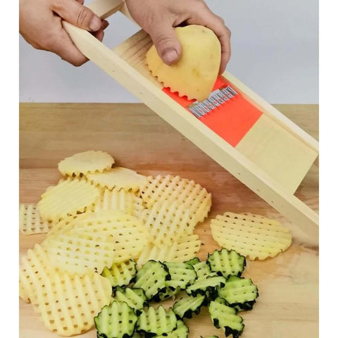 Wave waffle crinkle cutter with wooden frame and orange blade slicing a potato; crinkle-cut potato slices and zucchini on board.