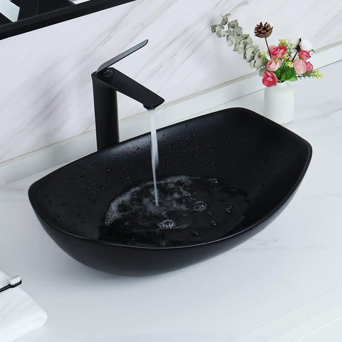 Matte black ceramic vessel sink with running water, featuring minimalist faucet on white countertop, contrasting design elements.
