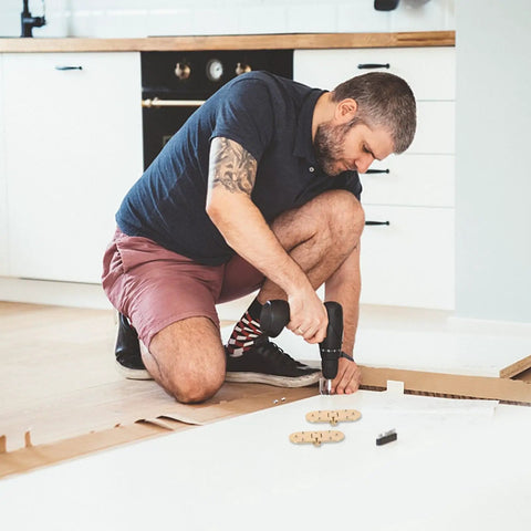 Man using drill to install brass table hinges 2-piece set for Butler tray and cabinet furniture on wooden floor