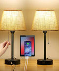 Bedside Table Lamps Set Of 2 With Dual USB Ports And Built In AC Outlet on wood surface, charging phone, fabric shades