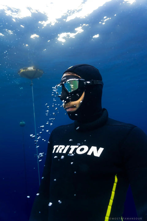 Diver underwater wearing a low volume freedive mask for freediving, spearfishing, and snorkeling with anti fog lens, black frame.