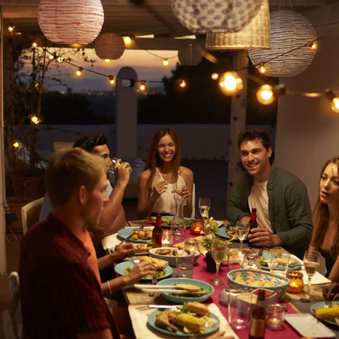 Outdoor string lights 150 ft with 75 shatterproof G40 bulbs illuminating a group dining on a porch in the evening