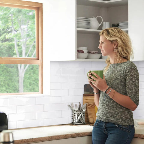 Woman in kitchen with X-Large Peel And Stick Backsplash Tiles, 5 Sheets Of 22.56 By 10.88 Inches, 3D Adhesive Wall Tiles visible