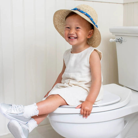 Smiling toddler wearing a hat on a toilet, using the Foldable Travel Potty Seat For Toddlers, Rock Solid And Slim Baby Toilet Training Chair For Road Trips, No Hassle Packable Design Made Right Here In The Usa.