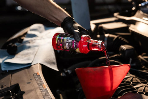 Shift Restore Transmission Additive 32 Oz being poured into a red funnel during car maintenance under the hood.