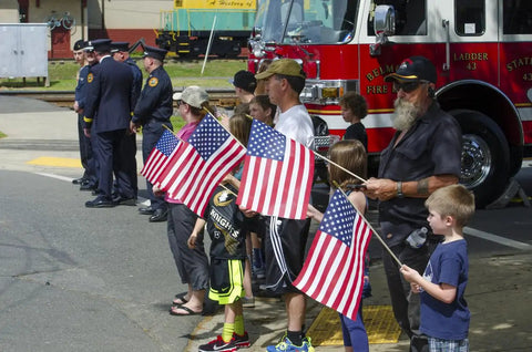 Children and adults hold 12 Pack 12x18 American Stick Flags With 30 Inch Wooden Poles And Gold Spear Tips Made In USA at a parade.