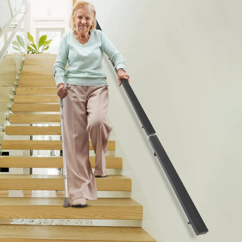 Wall Mounted Stair Handrail Crafted From Premium Stainless Steel Featuring A Sleek Black Square Profile Built Like A Tank For Indoor Spaces Loaded With Rock Solid Grip And Holds Down Weighty Loads Up To Two Hundred Pounds Safely, shown in use by elderly woman on staircase.