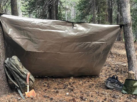 All Weather Survival Blanket With Reflective Heat set up as tarp in forest, desert camo 60 by 82 inches for outdoor adventures