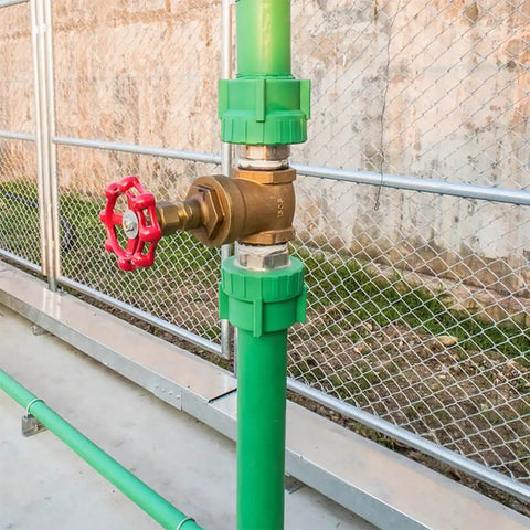 Green pipe with a red cast iron valve hand wheel handle, part of a 10 Pack Cast Iron Valve Hand Wheel Handles For Water Fittings With Reliable Sealing And Easy Open Close Flat Bottom Design For Garden Hose Valve Replacement And Durable Manual On Off Operation, near a chain-link fence