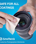Close-up of hands cleaning a camera lens with a beige SmoTecQ microfiber cloth; blue background.
