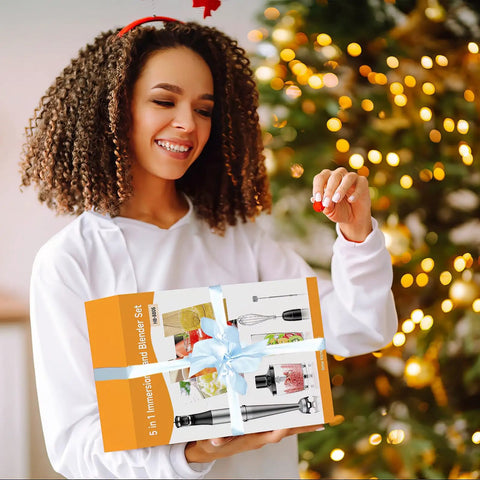 Happy person holding a wrapped 5-in-1 immersion blender set by the Christmas tree, featuring the Heavy Duty Immersion Blender Handheld Corded 1100W.