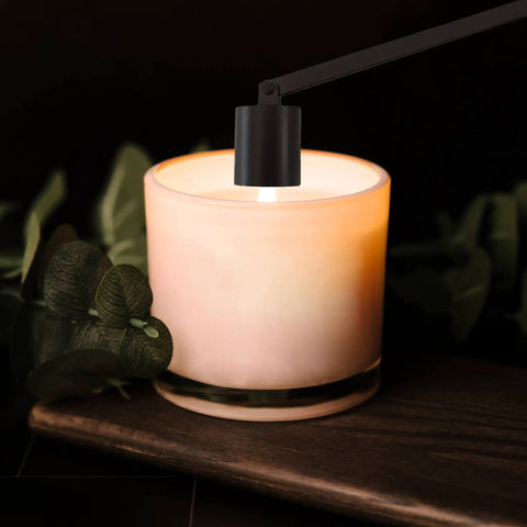 Sleek Black Stainless Steel Candle Snuffer With Rotating Swivel Bell And Ergonomic Grip Handle For Smooth Flame Control And Deep Jar Reach near a lit candle.