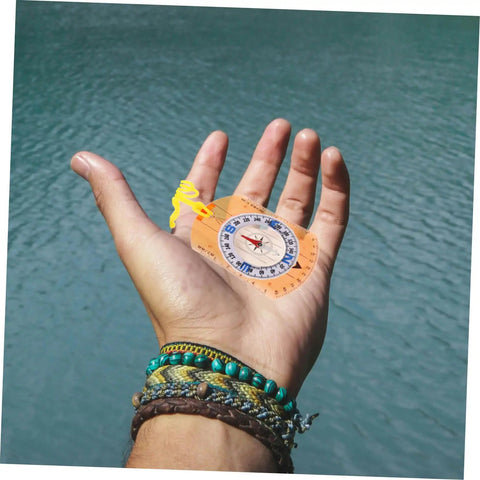 Trail Ready Orienteering Compass With Multi Function Built In Ruler Pointer And Luminous North held in hand, next to water