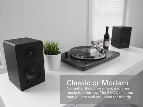 PB42X Powered Bookshelf Speakers with 30 Watt RMS near a record player on a modern white shelf in a home studio setup