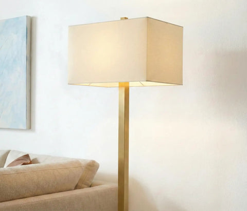 Stella Brass Floor Lamp With Modern Mid Century Vibe For Living Rooms And Offices, tall design with beige shade near sofa.