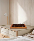 Top Shelf Solid Walnut Wood Jewelry Tray Organizer With Fifteen Grids For Rings Necklaces And Bracelets Compact Vanity Storage Display Plate For Counters on a bedside table.