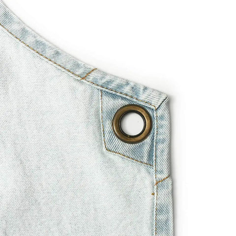 Close-up of light blue cotton denim with metal grommet detail on Denim Tool Shop Apron For Hairstylists With Five Pockets, Cross Back Straps.
