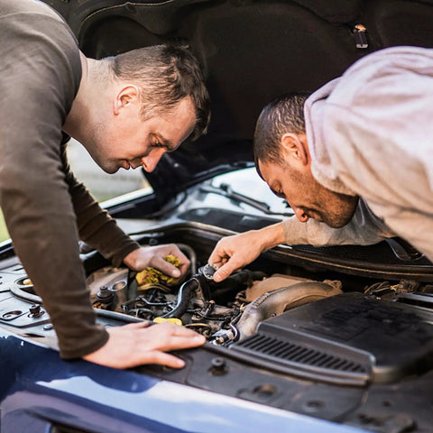 Two men inspecting a car engine under an open hood, focusing on automotive maintenance and repair work.