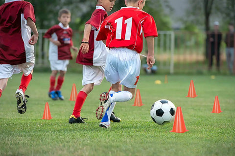 Kids playing soccer with 12 Inch Traffic Training Sports Cones 10 Pack Or 24 Pack Orange Safety Markers on grass field