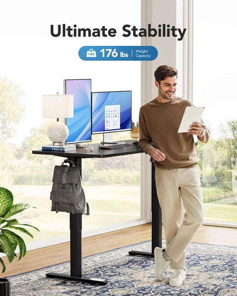 Man using Electric Standing Desk With Real Deal One Piece Desktop Adjustable Height For Sit Stand Four Memory Settings 48 By 24 Inches Heavy Duty Steel Frame Built To Last Home Office Desk Black in modern setting