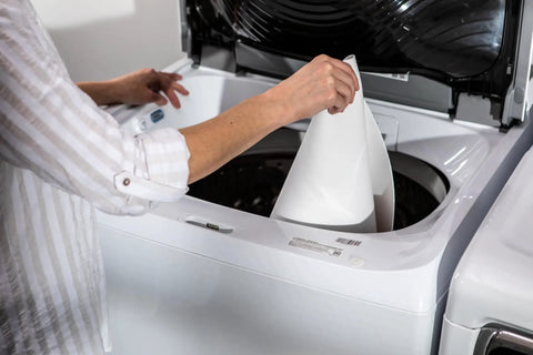 Non Adhesive Shelf Liners For Kitchen Cabinets And Pantry Wire Shelving Featuring A Solid Grip Base Locking Items In Place And Keeping Craziness Contained Machine Washable White 6 Roll Pack being placed in a washing machine.