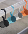 Four XB100 Wireless Bluetooth Portable Speakers in black, blue, gray, and orange with straps hanging on a rod