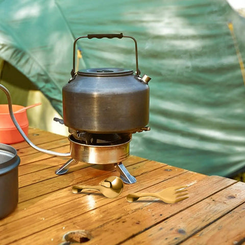 Camping kettle and portable stainless steel camp utensils set with pink organizer case on wooden table outdoors.