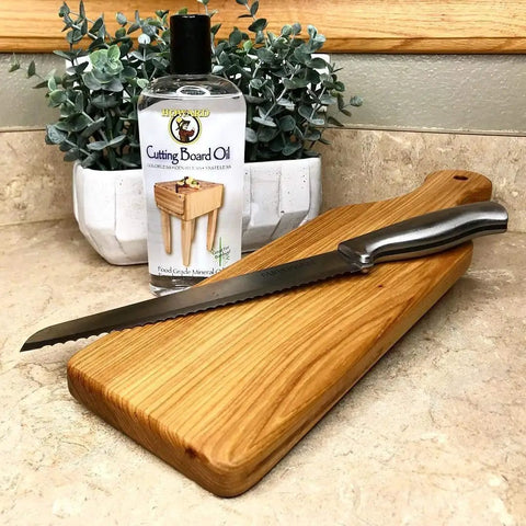 Butcher Block And Cutting Board Oil 12 Oz Pack Of 3 Colorless Odorless Tasteless Food Safe With Vitamin E FDA Approved For Food Contact positioned next to a serrated knife on a wood cutting board.