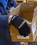 Person wearing box handling work gloves with extreme grip and performance fit holding a cardboard box in a warehouse.