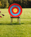 Three traditional handmade archery targets with straw core for backyard practice, arrows in left target, green field background.