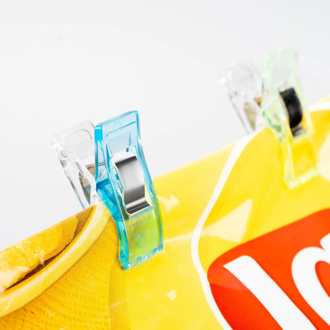 Super Handy Pack Of 100 Clear Plastic Sewing Clips holding fabric with a colorful design, showcasing their clear and sturdy build.