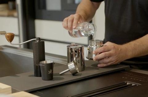 Hella Durable Stainless Steel Stovetop Espresso Maker For Rich Coffee Brews pouring water into moka pot in kitchen.