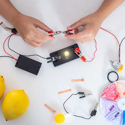 Hands connecting E10 Screw Base Miniature Bulbs For DC 12V Projects Packing Ten Warm Yellow Glow to a battery with clips.