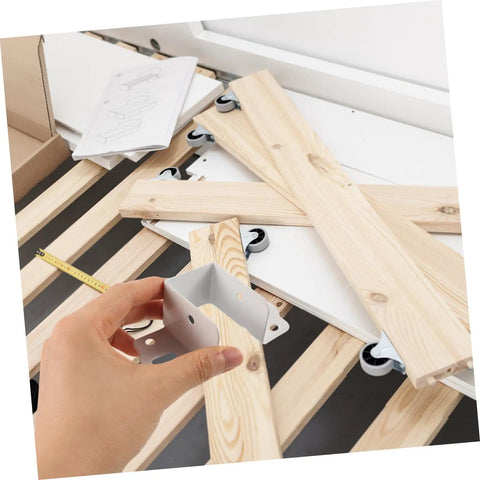 Hand holding a metal connector for bed frames atop wooden slats, part of the Built Tough Metal Bed Rail Fasteners Twenty Piece Hinge Buckles And Snappy Slide Hooks For No Sweat Bed Frame Setup Solid Fit Furniture Bracket Hardware Kit.
