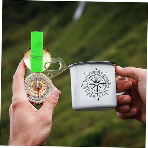 Person holding thumb type directional compass for outdoor navigation and a mug in nature scene.