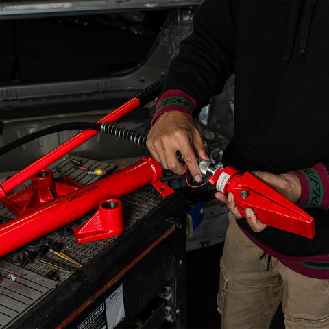 10 Ton Hydraulic Porta Power Jack Ram being used with red attachments on a workshop table for auto body frame repairs.