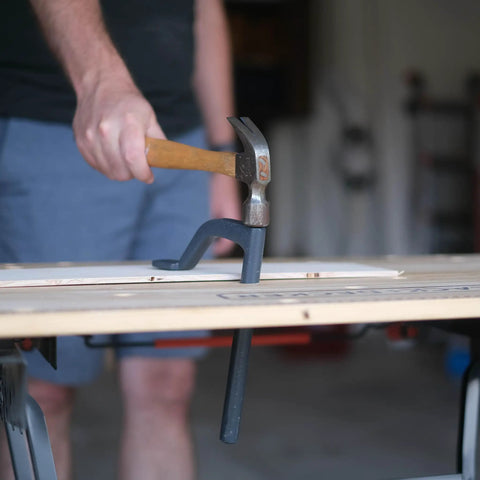 Man using hammer to secure 8 Inch Bench Holdfast Clamps for Woodworking, Heavy Duty Hold Downs, featured on workbench during use