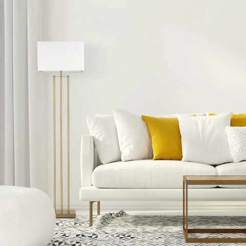 Room with SoHo Floor Lamp 62 Inch In Matte Brass With White Linen Shade next to a white sofa with yellow pillows.