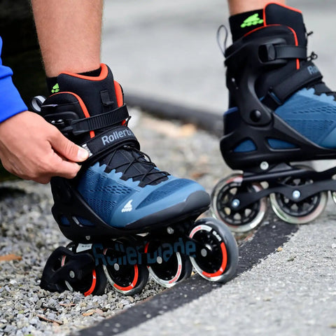 Person fastening Macroblade 90 Fitness Inline Skates For Adults Unisex With Dope Lateral Support And Stability High Cuff Flex Orion Blue Orange Size 38 Built For Speed And Training Skating on their feet, showcasing the blue and orange design and 90mm wheels on a path.