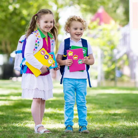 Children holding notebooks with 90Pcs Hibiscus Flower Name Tag Stickers Set With 9 Dope Styles Colorful Floral Blank Nameplates in a park.
